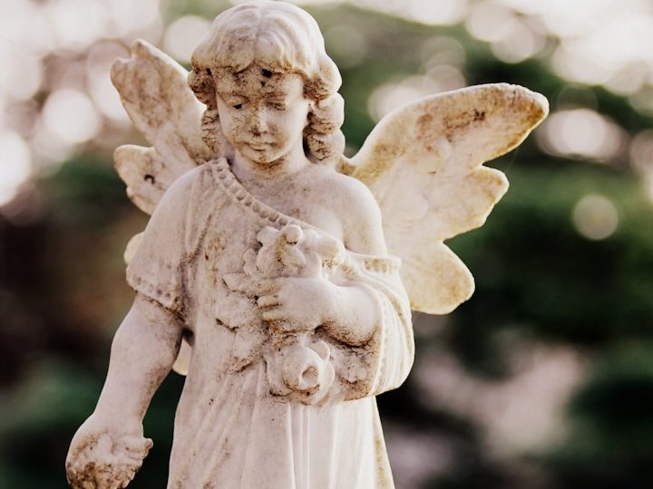 Skulptur eines Engels mit Flügeln, der ein Kind und Blumen hält.