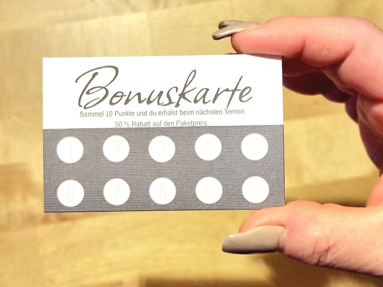 Hand hält eine Bonuskarte mit grauem Design und weißen Punkten.