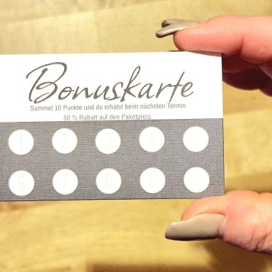 Hand hält eine Bonuskarte mit weißen Punkten auf grauem Hintergrund.