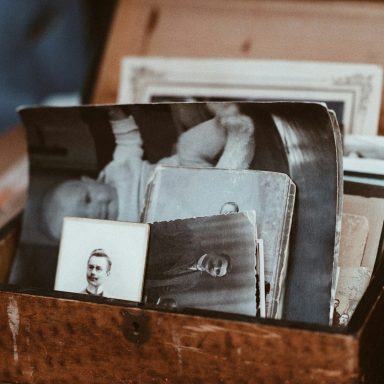 Eine Holzkiste mit alten Fotos, darunter ein Bild eines Babys und ein Porträt eines Mannes.