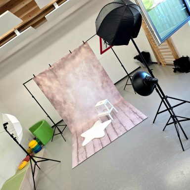 Fotostudio mit einem Hintergrund, einem Stuhl und Beleuchtungsausrüstung.