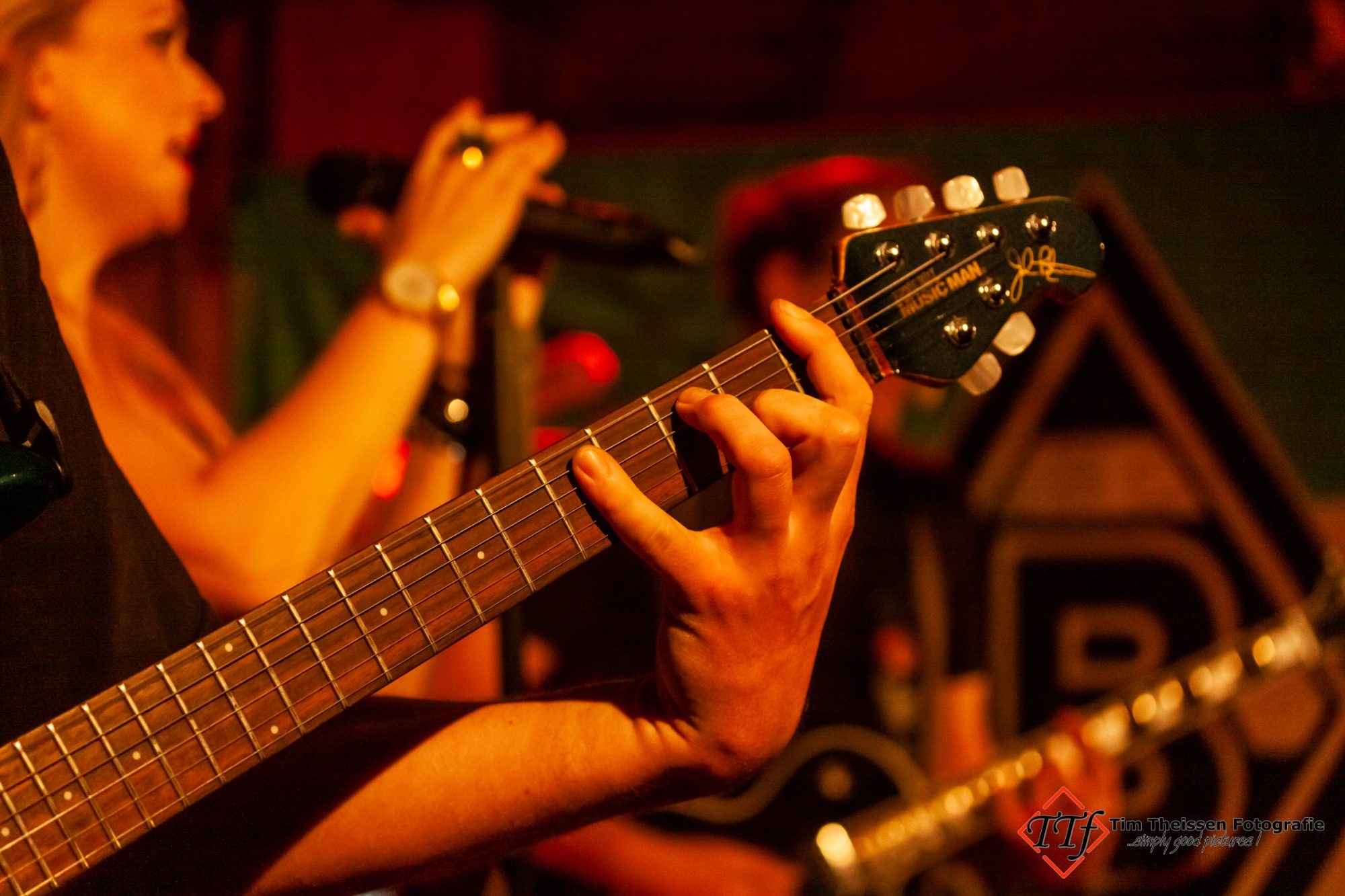 Eventfotos Eine Hand spielt Gitarre, während im Hintergrund ein Gesang zu hören ist.