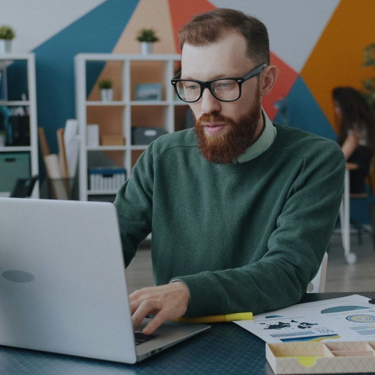 Mitarbeiter Mann mit Bart und Brille sitzt am Laptop und arbeitet