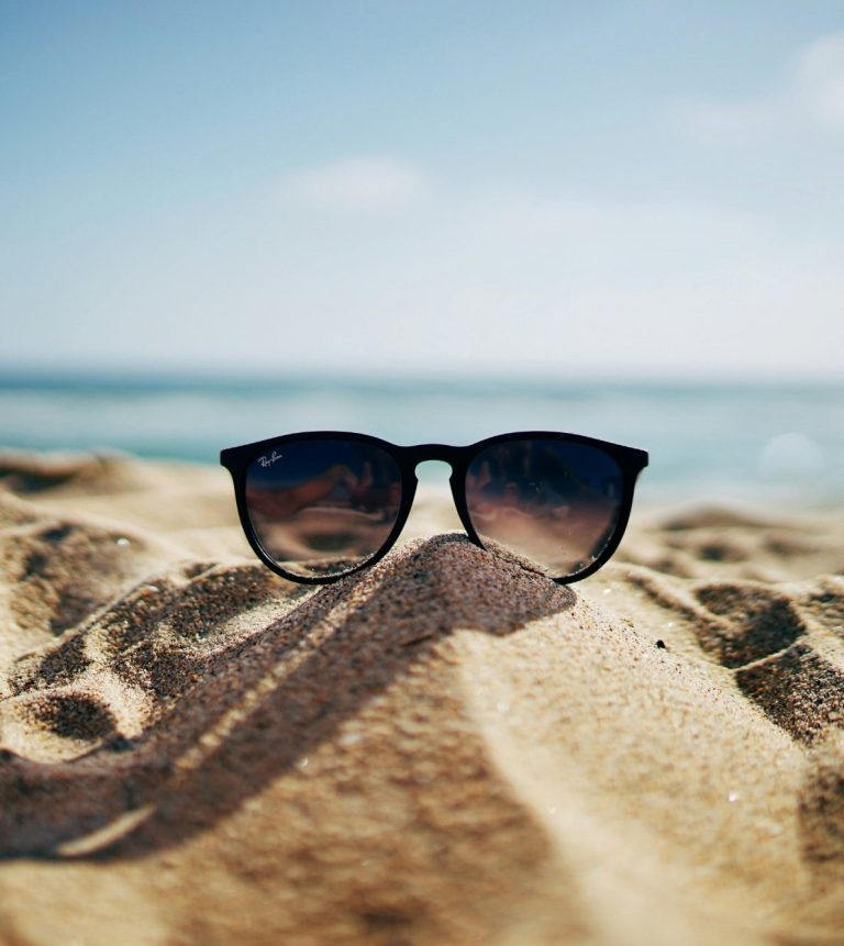 Sonnenbrille liegt im Sand am Strand mit Meer im Hintergrund.