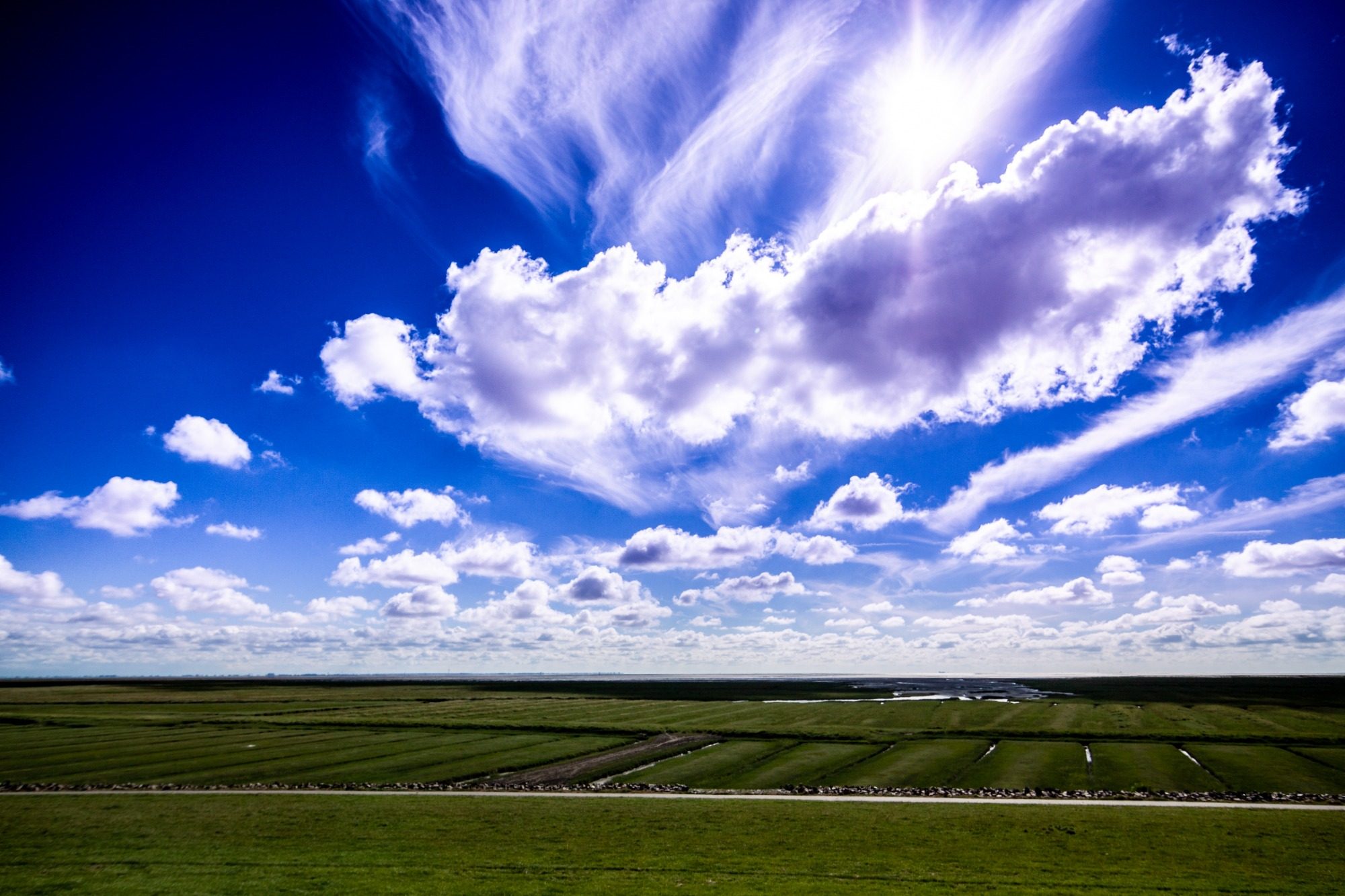 Landschaftsfotos Blauer Himmel mit weißen Wolken über einer weiten grünen Landschaft.
