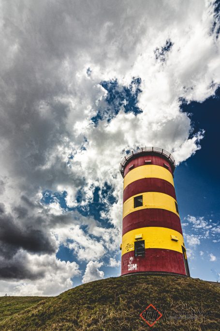 Bunter Leuchtturm auf einem Hügel unter einem bewölkten Himmel.