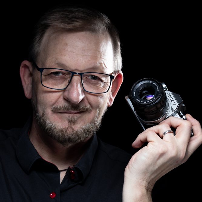 Tim Theissen Fotografie Mann mit Bart und Brille hält Kamera