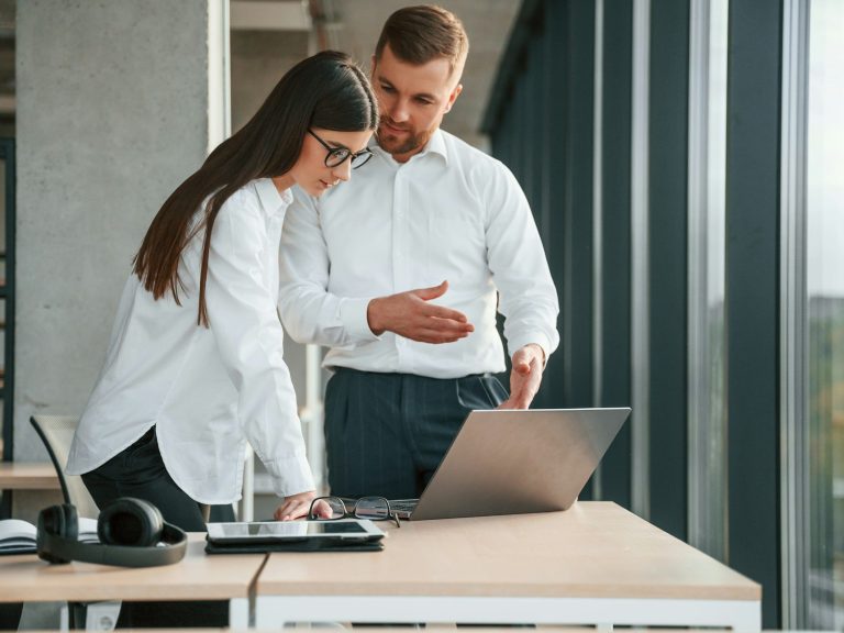 Recruting Mann und Frau mit weißen Hemden stehen an Schreibtisch vor Laptop