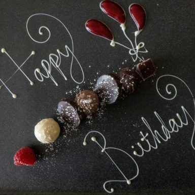 Schokoladendesserts mit der Aufschrift „Happy Birthday“ und Luftballons aus Glas.