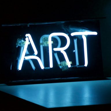 Leuchtendes Neonzeichen mit dem Wort "ART" in blauer Schrift.