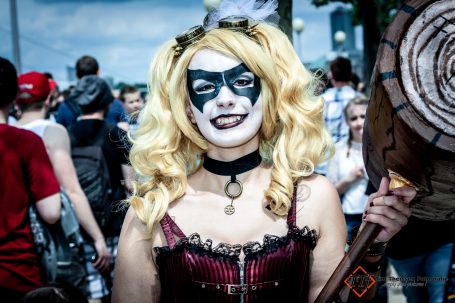 Frau in einem kostüm mit Harlekin-Make-up, blonden Locken und einer Axt.