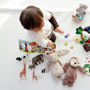 Ein Baby spielt mit Tierfiguren und Plüschtieren auf einem weißen Teppich.