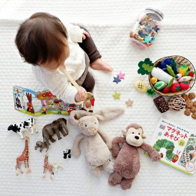 Ein Kleinkind spielt mit Spielzeug, Bücher und Stofftiere auf einer Decke.