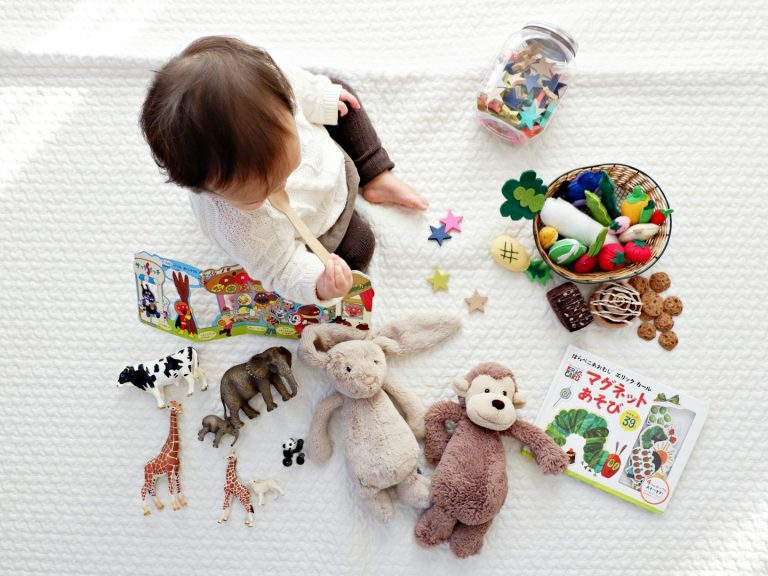 Ein Kleinkind spielt mit Tierfiguren, Plüschtieren und bunten Spielsachen.