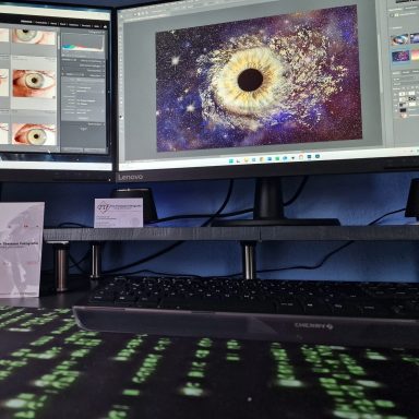 Zwei Computerbildschirme zeigen grafische Designs und Programmiercode auf einem Tisch.