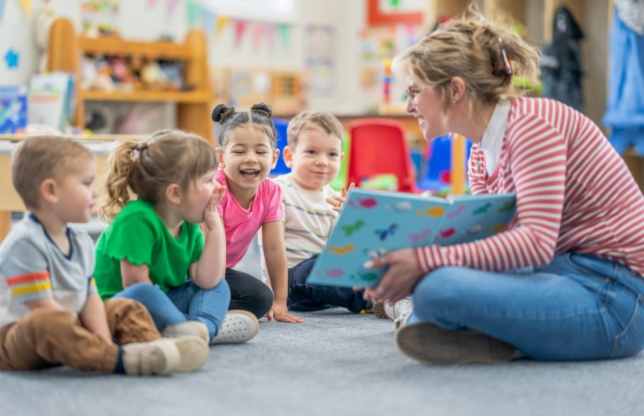 Kinder und Erzieherin sitzen auf dem Boden und lesen eine Geschichte