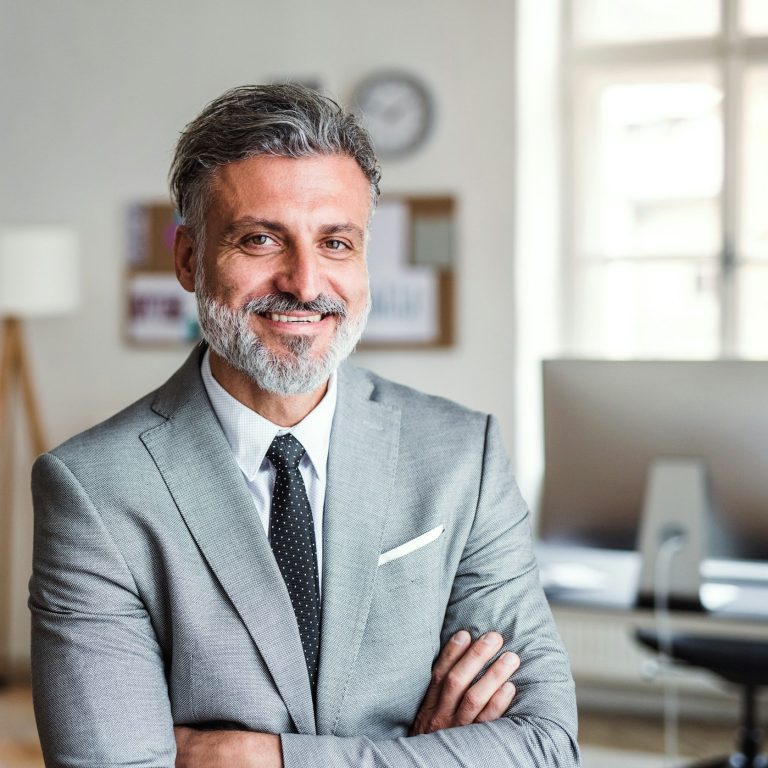 Business Fotografie Mann mit grauen Bart und Haaren lächelt im Anzug in die Kamera