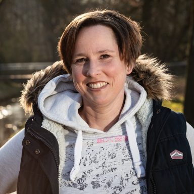Frau mit kurzer Frisur, lächelt, trägt eine dunkelblaue Weste und einen grauen Hoodie.