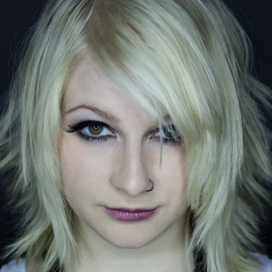 Junge Frau mit blonden, zerzausten Haaren und intensiven Augenblick. Scharfer Blick.