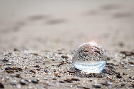 Glaskugel auf sandigem Boden, reflektiert Licht und Umgebung.