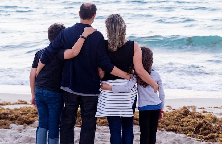 Familie steht am Strand und schaut aufs Meer hinaus