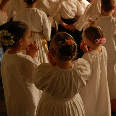 Kinder in weißen Kleidern mit Blumen im Haar, stehen in einer versammelten Gruppe.