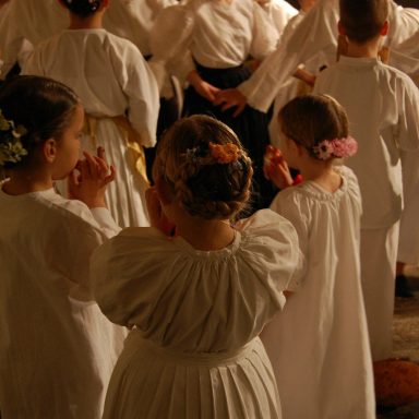 Kinder in weißen Kleidern bei einer Feier, einige mit Blumen im Haar.