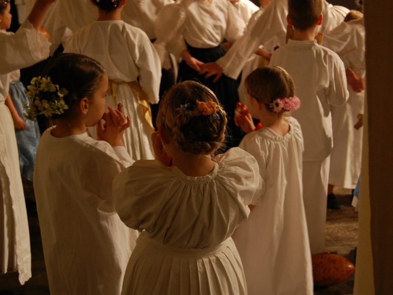 Kinder in weißen Kleidern mit Blumen im Haar, bei einer feierlichen Veranstaltung.