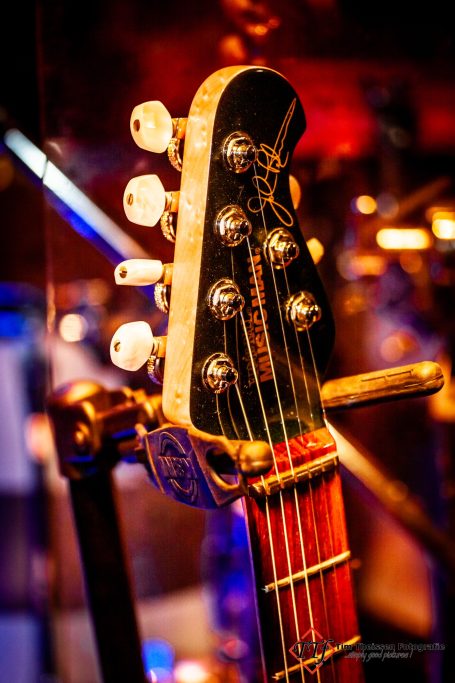 Nahaufnahme eines Gitarrenhalses mit Kopfplatte und Stahlseiten in buntem Licht.