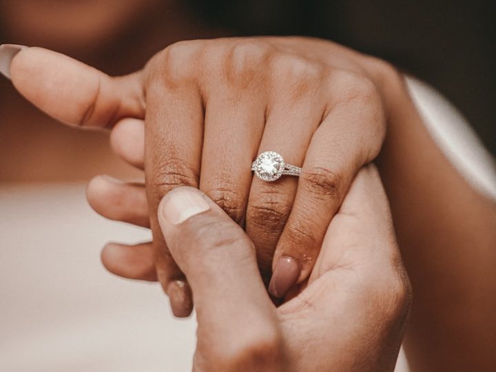 Eine Hand hält eine andere, die einen klassischen Verlobungsring trägt.