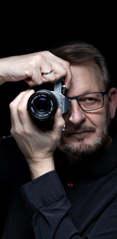 Mann mit Brille hält eine Kamera mit einer Hand und blickt durch den Sucher.