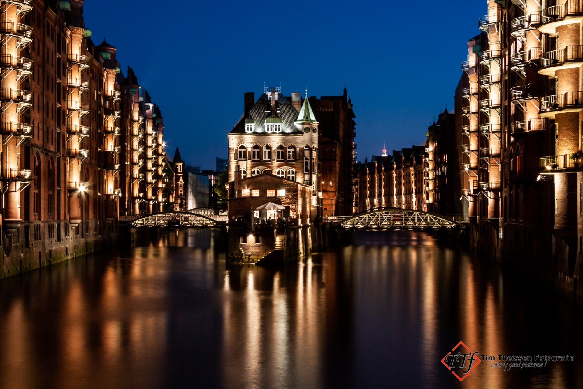 Stadtfotos Beleuchtete Speicherstadt bei Nacht mit ruhigem Kanal und historischen Lagerhäusern.