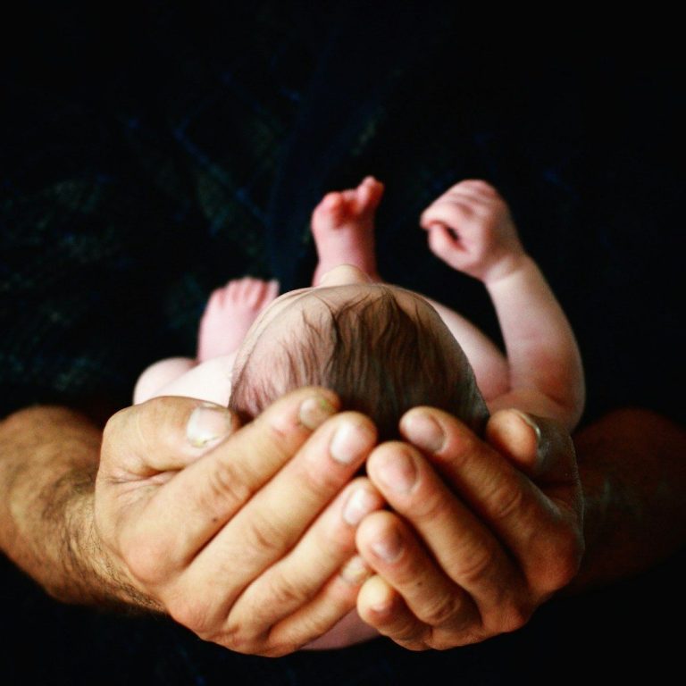 Baby Shooting Mann hält mit seinen zwei Händen ein neugeborenes Kind
