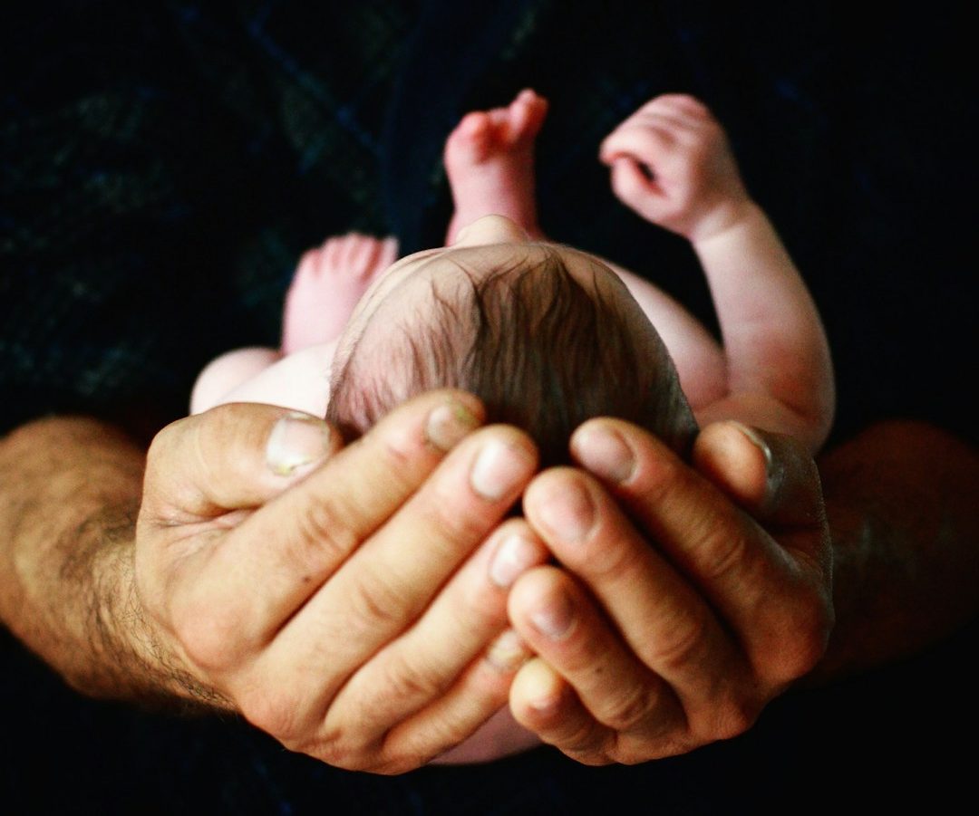 Newborn Neugeborenes Kind wird in den Händen vom Vater gehalten.