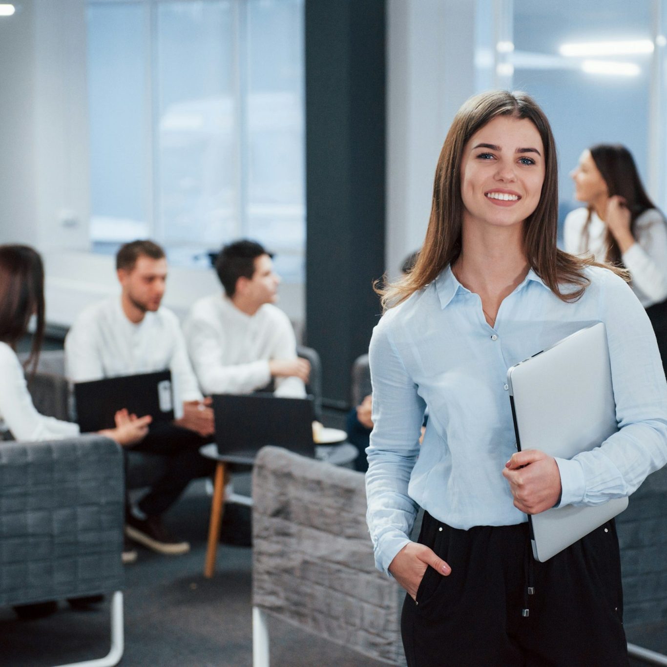 Businessfrau mit Langen Haaren steht mit Laptop unterm Arm im Büro