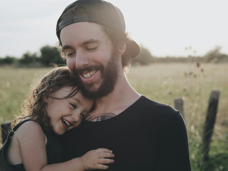 Ein lächelnder Vater umarmt sein lachendes Kind auf einer Wiese.