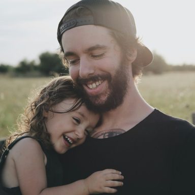 Vater umarmt lachendes Kind in einem Feld bei Sonnenuntergang.