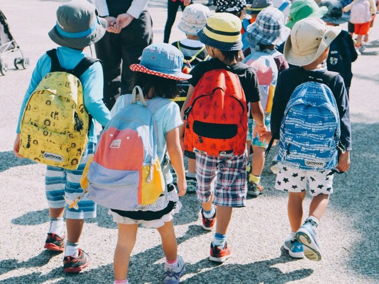 Gruppe von Kindern mit bunten Rucksäcken und Hüten, die gemeinsam gehen.