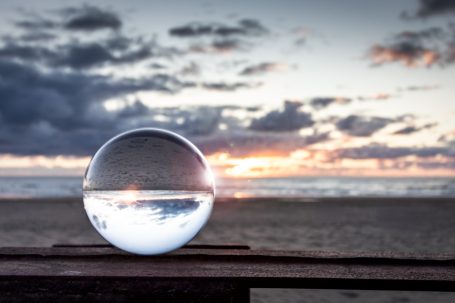 Glaskugel auf einem Holztisch, reflektiert Sonnenuntergang am Strand.